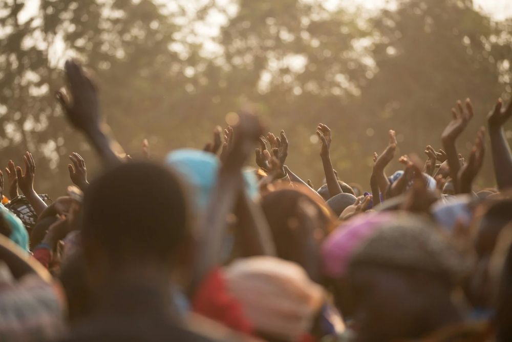 A large crowd with hands raised in worship, lit by warm sunlight