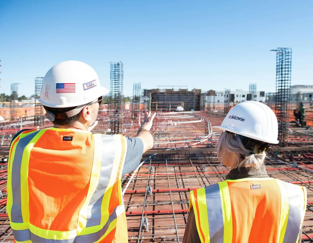 Two workers in hard hats and safety vests looking out over a construction site