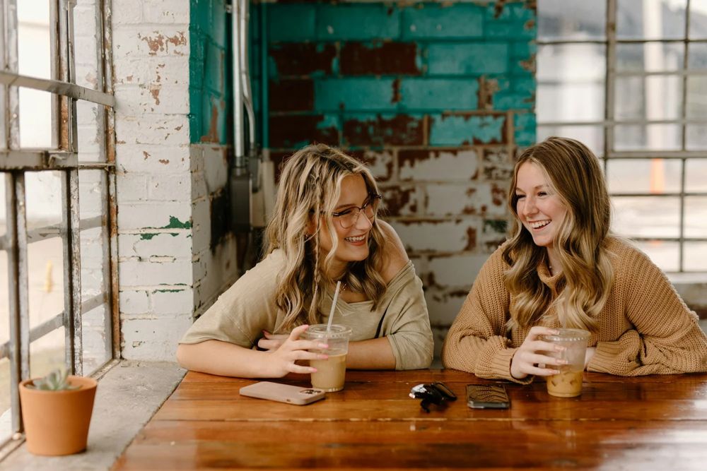 Two young women talking and laughing over coffee at a wooden table